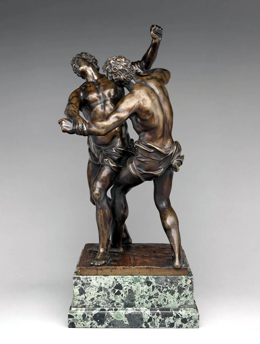 Ancient bronze statue of two men standing while wrestling attached to a marble base.