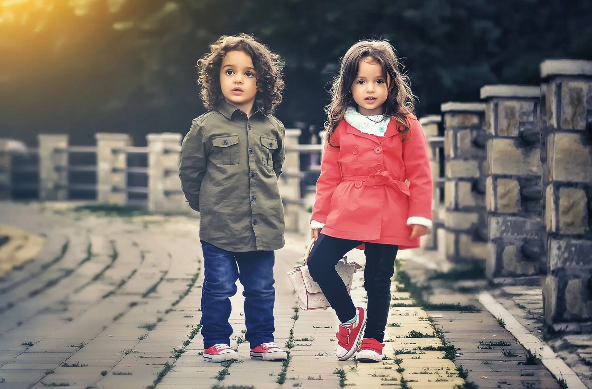 Two children wearing coats standing on a walkway while looking into the camera