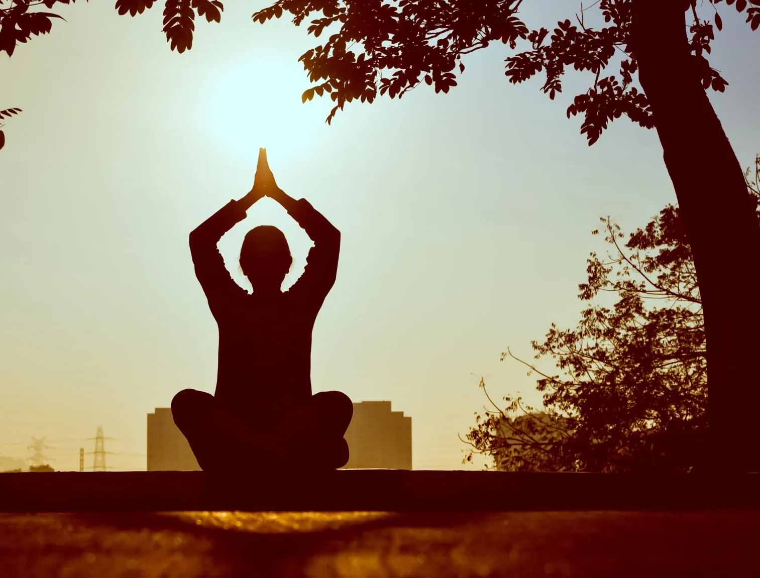 Silhouette of a woman performing a meditation pose with her hands joined together above her head