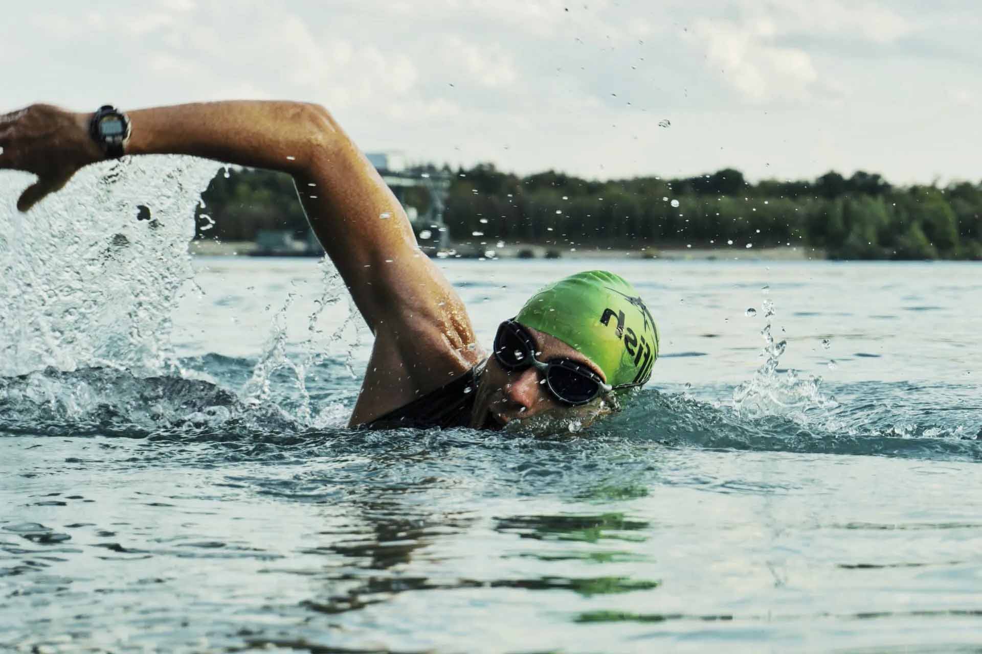 Professional swimmer in water in the middle of a stroke wearing swimmers cap and goggles