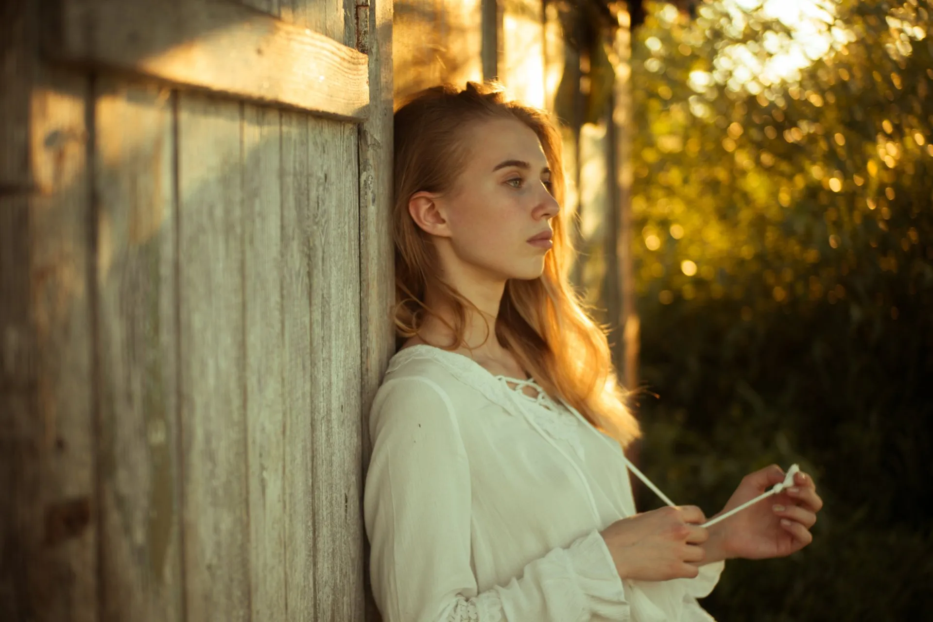 Woman leaning her back onto wooden door with a sadden face looking off into the distance