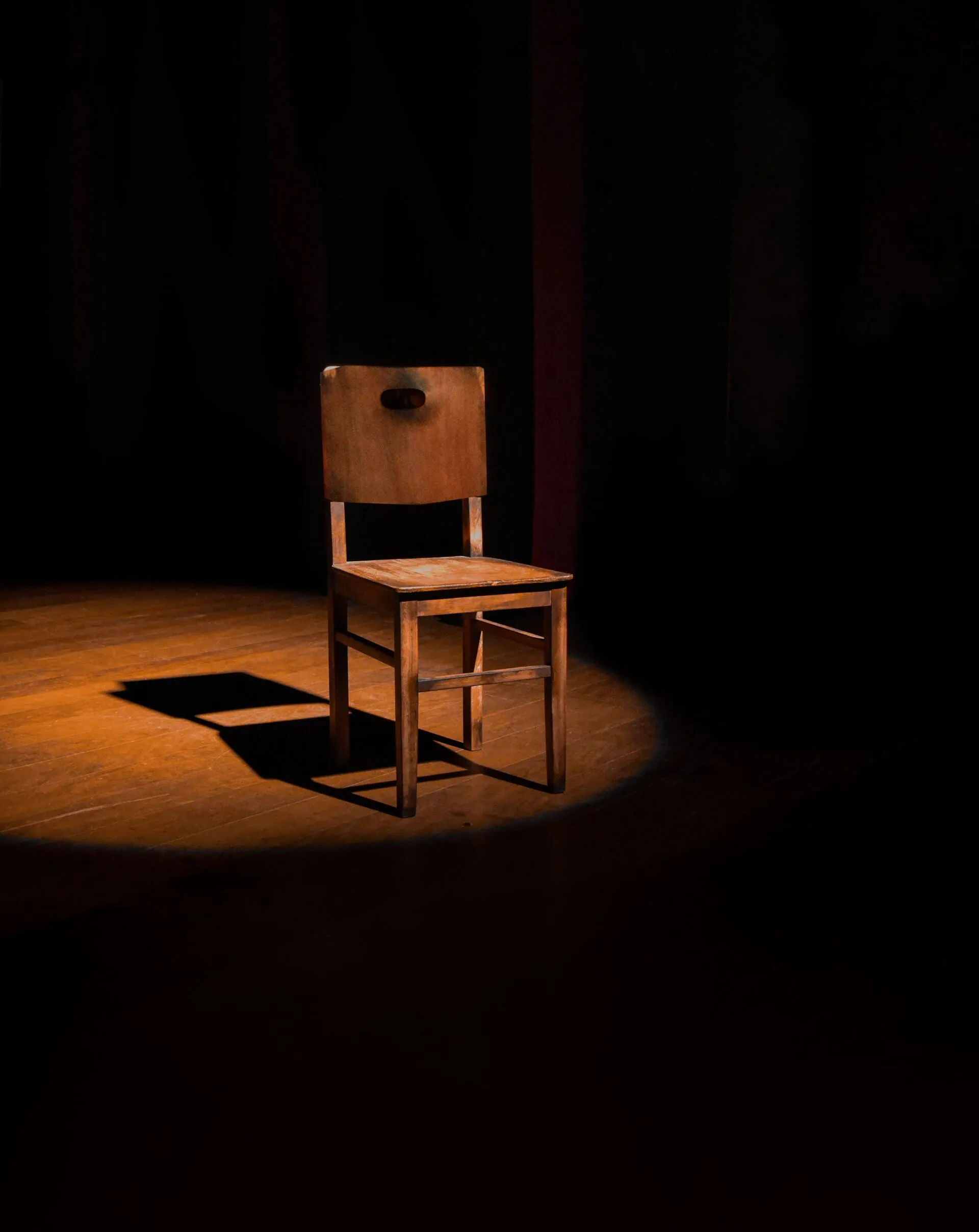 Old wooden chair sitting in the spotlight of a dark stage