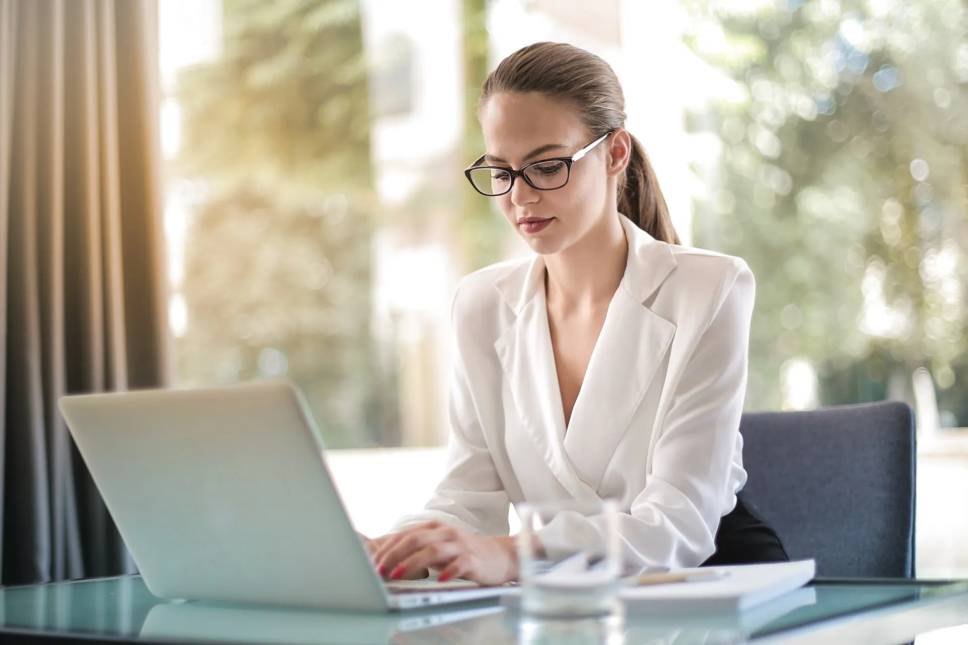 Woman wearing glasses sitting at a desk typing on her laptop