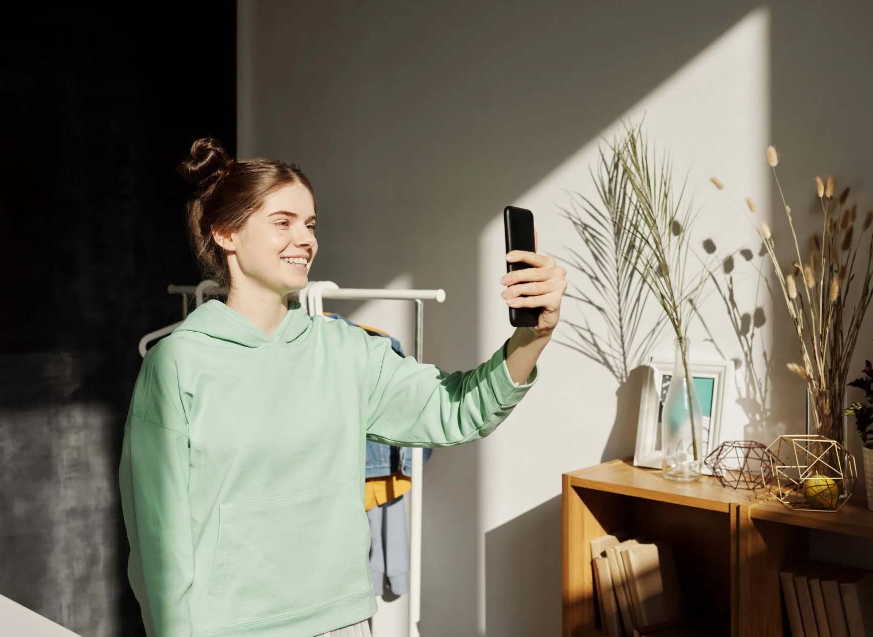 Young woman in green sweatshirt holding up her phone to take a selfie