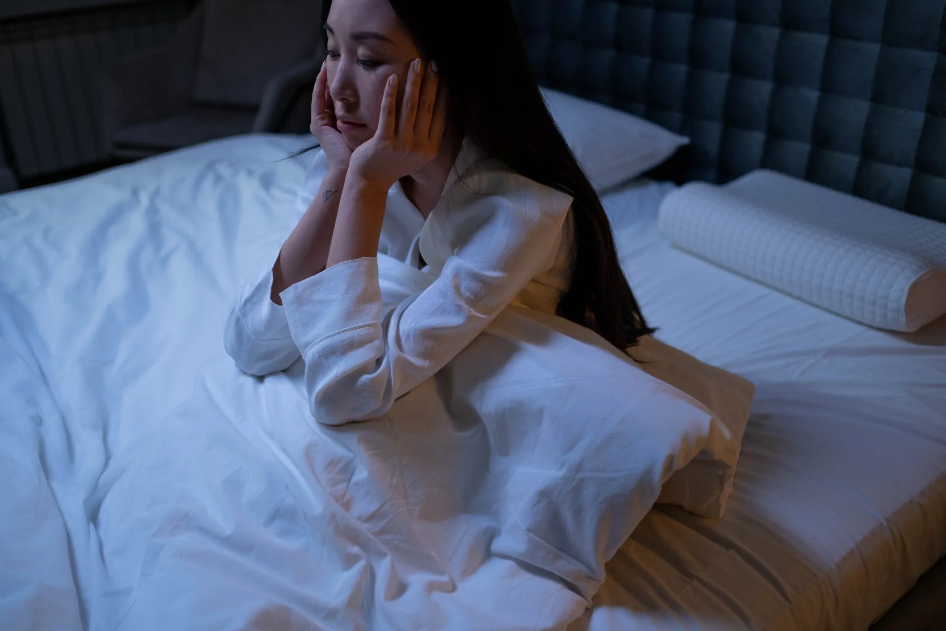 Woman sitting up on bed with bed covers over her legs with a stressed loook on her face