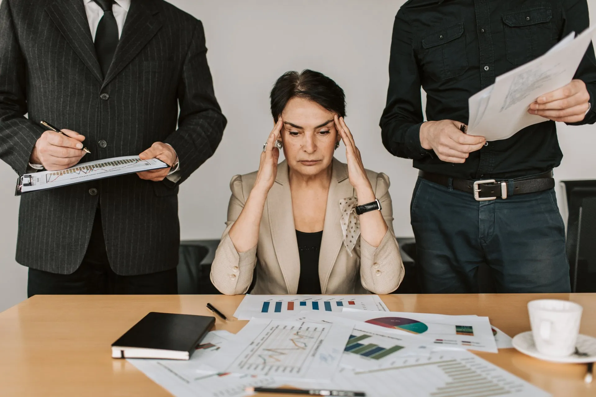 Woman in tan suit jacket rubbing the temple of her head due to stress