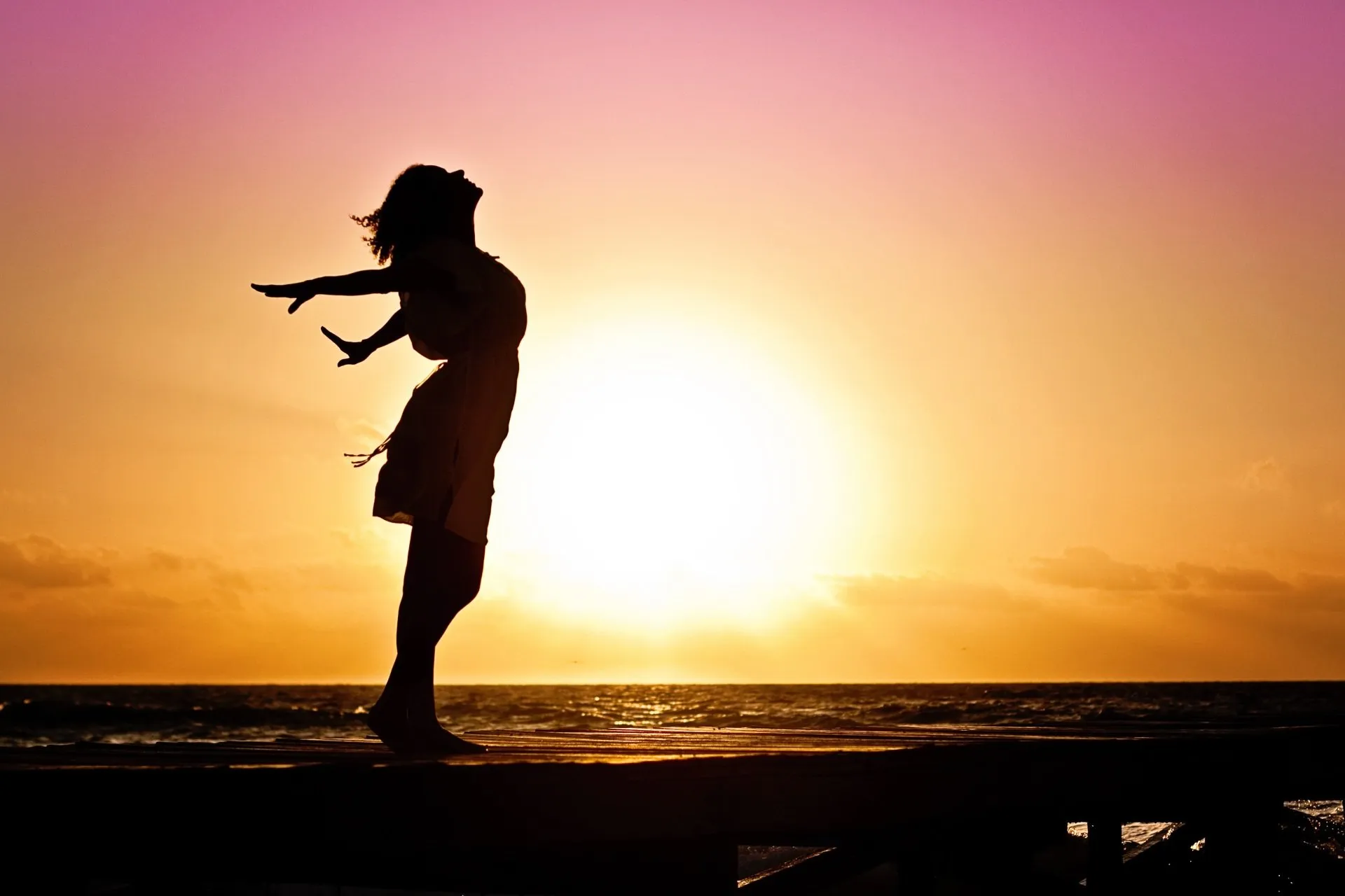 Silhouette of woman on beach with her arms spread wide showing a sense of freedom