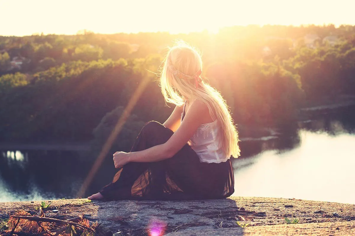 Woman sitting on a rock looking out over a river with the sun in the background